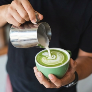 Professional barista pouring steamed milk into matcha tea to create latte art, demonstrating excellent color retention.