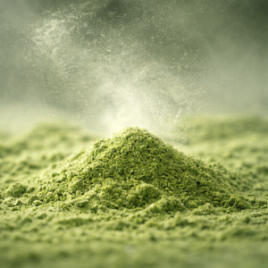 Macro close-up of finely ground matcha powder with a soft dust plume in natural light, highlighting ultra-fine grinding quality.