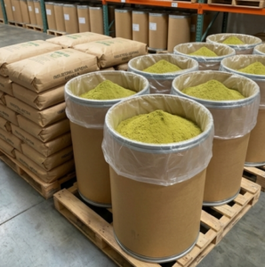 Large industrial fiber drums and bulk bags of matcha powder in a warehouse for food processing factories.